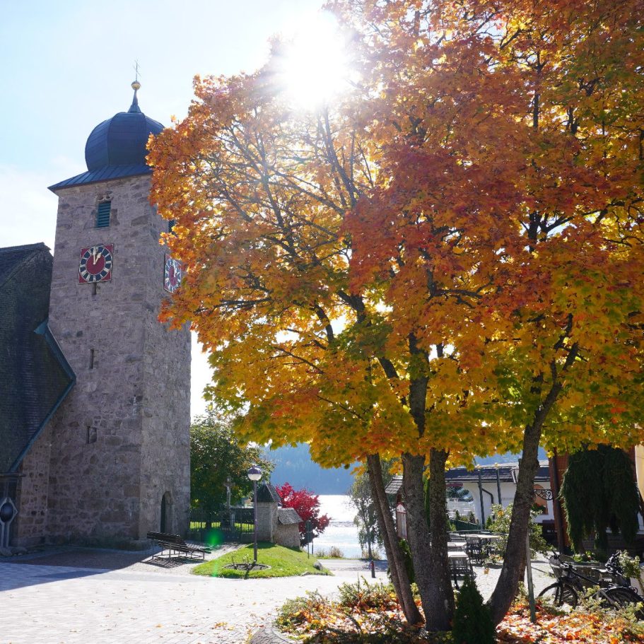 Bunte Herbstbäume vor einer alten steinernen Kirche am Wasser.