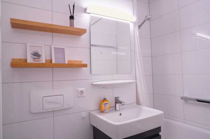 Modernes Badezimmer mit Waschbecken, Spiegel und Regalen aus Holz.