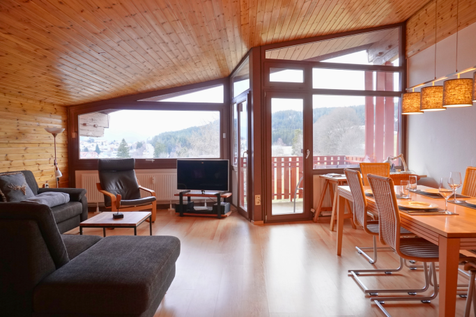 Modern Wohnraum mit Holzdecke, gemütlichen Möbeln und großen Fenstern.