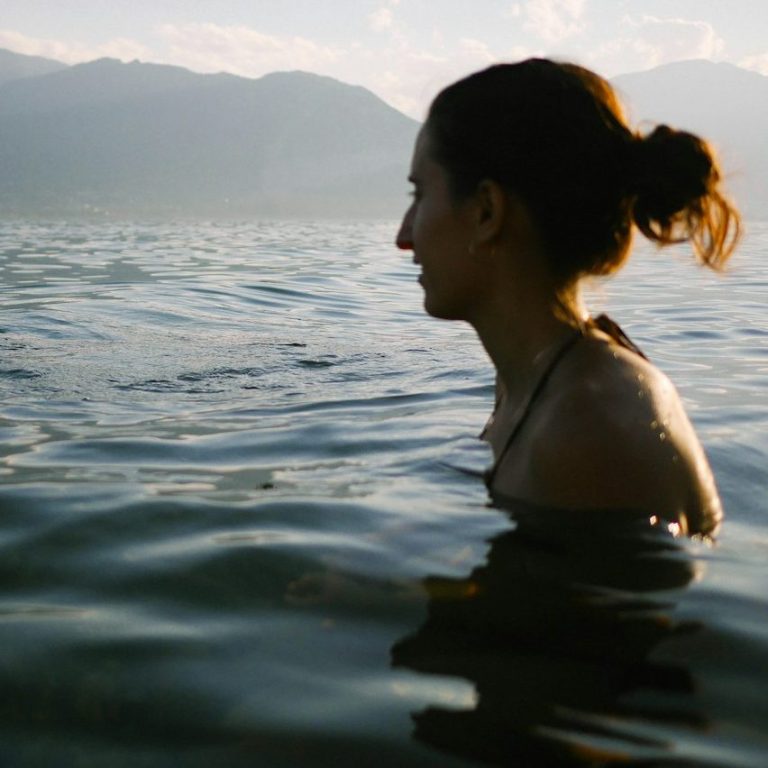 Frau steht im Wasser, umgeben von Bergen und einer wolkigen Himmelshorizont.