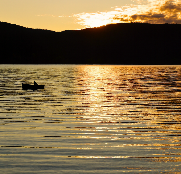 Sonnenuntergang am Schluchsee Ein Mensch sitzt in einem Boot auf ruhigem Wasser bei Sonnenuntergang.