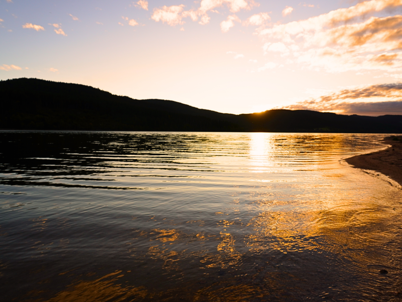 Sonnenuntergang über einem ruhigen See mit Bergsilhouette im Hintergrund.