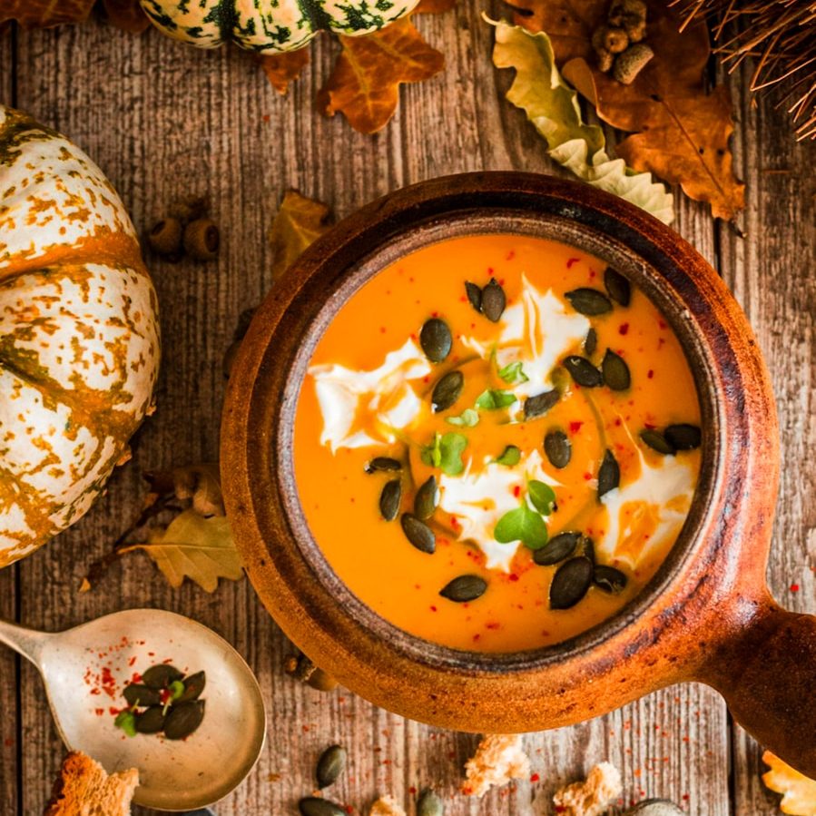 Kürbissuppe in einer Holzschüssel, garniert mit Sahne und Kürbiskernen, umgeben von Herbstdekor.