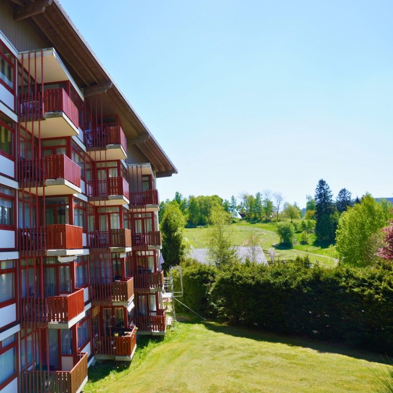Ferienressort Kurhotel Schluchsee Moderne Appartementanlage mit rotem Balkon und grünem Garten im Hintergrund.