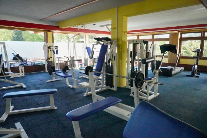 Fitnessstudio mit mehreren Geräten und Gewichten, in einem hellen Raum.