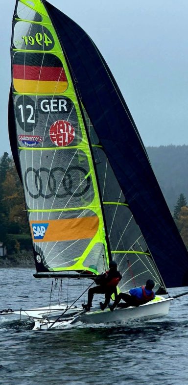 Segelboot mit Segler auf dem Schluchsee, Wind in den Segeln, grauer Himmel im Hintergrund.