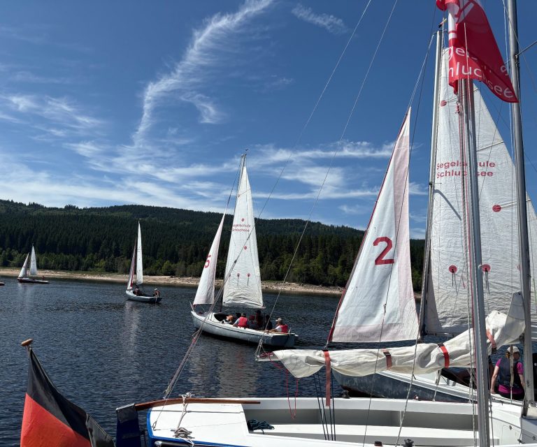 Segelboote auf dem Schluchsee unter einem klaren blauen Himmel mit bewaldeten Hügeln im Hintergrund.