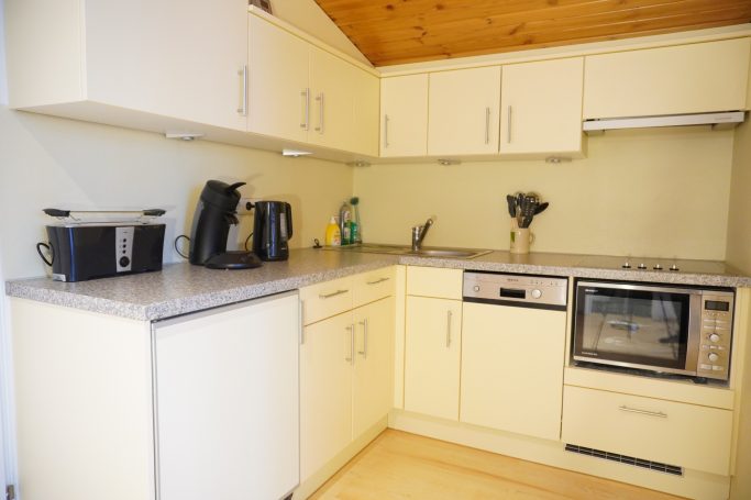 Helle Küche mit Kaffeemaschine, Wasserkocher, Kühlschrank und Backofen.