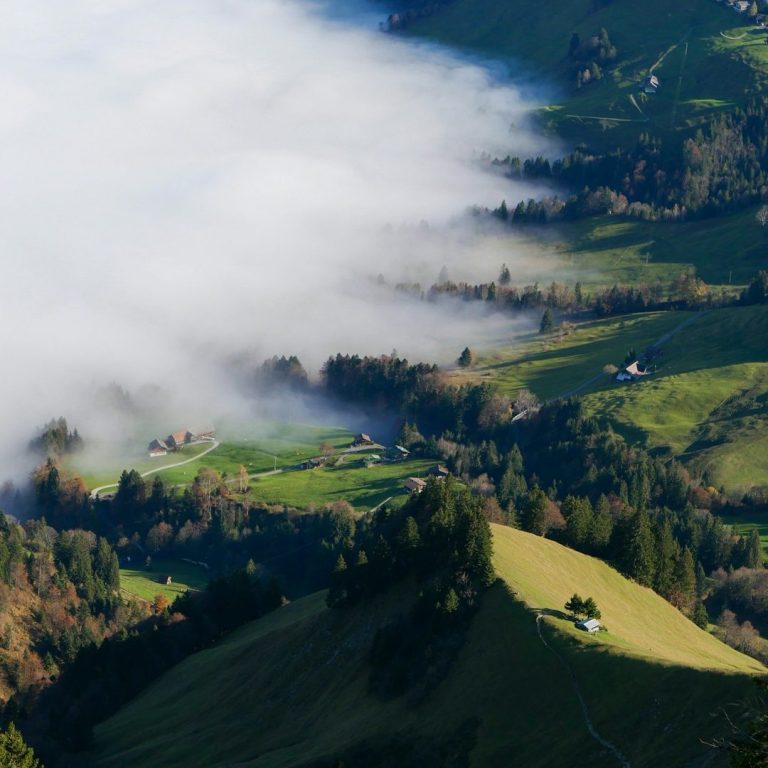 Berglandschaft mit grünem Tal, Nebel und verstreuten Häusern.
