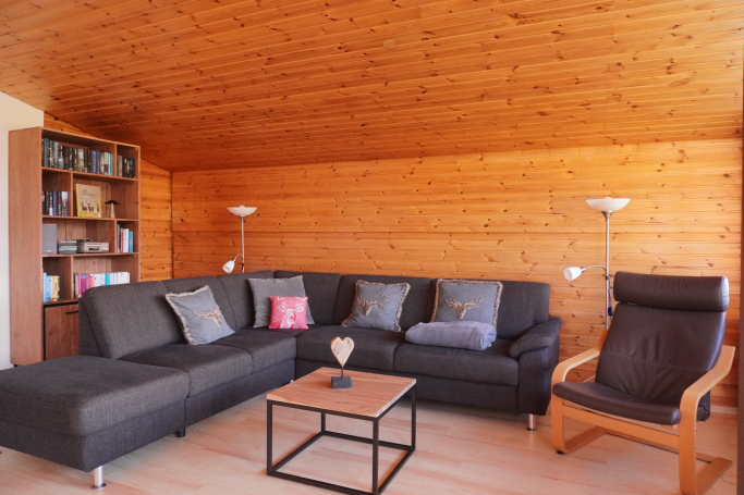 Gemütliches Wohnzimmer mit einer Couch, Sessel und Holzwänden. Tisch in der Mitte.