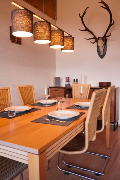 Holztisch mit stilvollen Stühlen, beleuchtet von modernen Lampen und Dekoration mit Geweih.