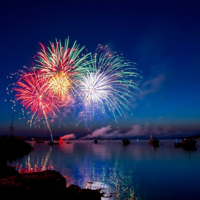 Bunte Feuerwerke spiegeln sich im ruhigen Wasser eines Gewässers bei Nacht.
