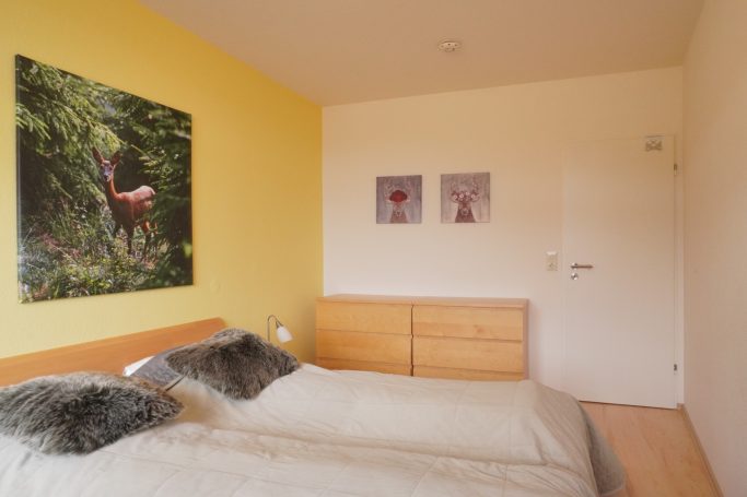 Schlafzimmer mit gelber Wand, zwei Betten und Naturbildern.