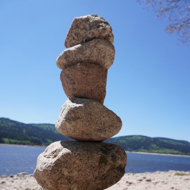 Fünf Steine sind übereinander gestapelt, vor einem klaren Himmel und Wasser.