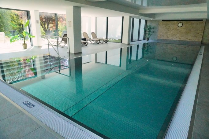 Innenpool mit klarem Wasser und großen Fenstern, umgeben von Pflanzen.