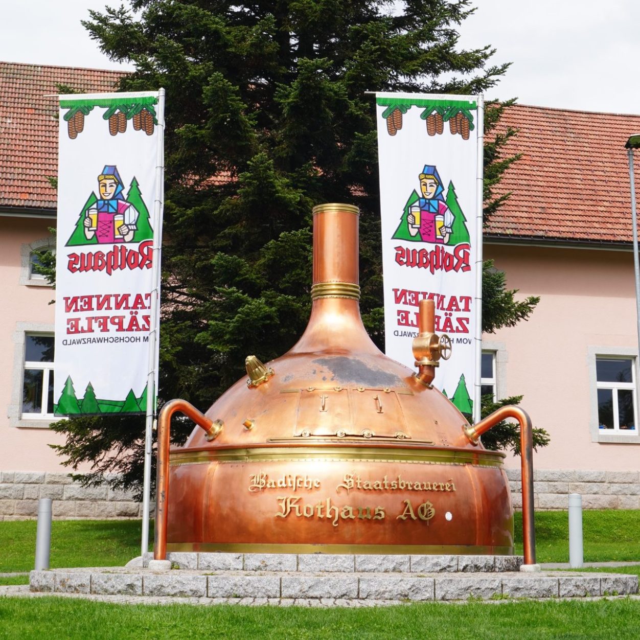 Rothaus Brauerei Kupferne Sudpfanne vor einem Gebäude mit Werbebannern.