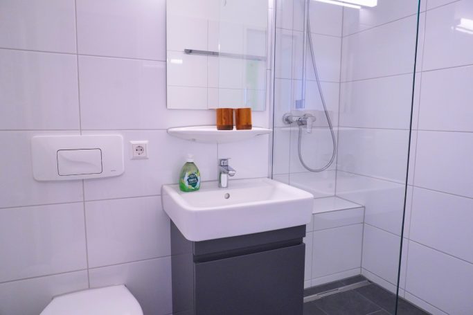 Moderne Badezimmer mit Dusche, Waschbecken und weißen Fliesen.